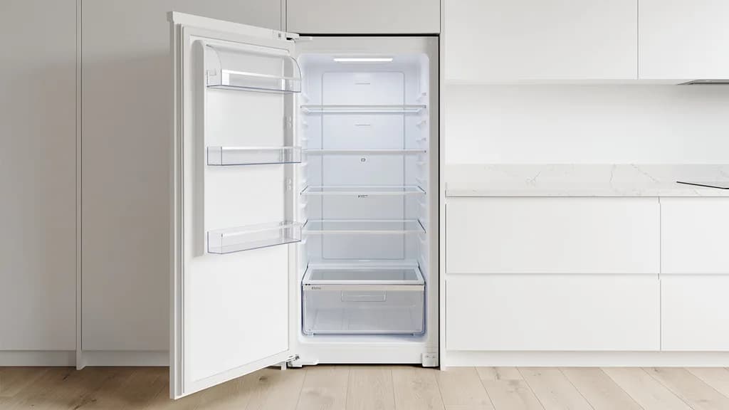Geöffneter Einbaukühlschrank mit vier leeren Glasablagen, Gemüsefach und Türfächern in einer weißen Küchenzeile.