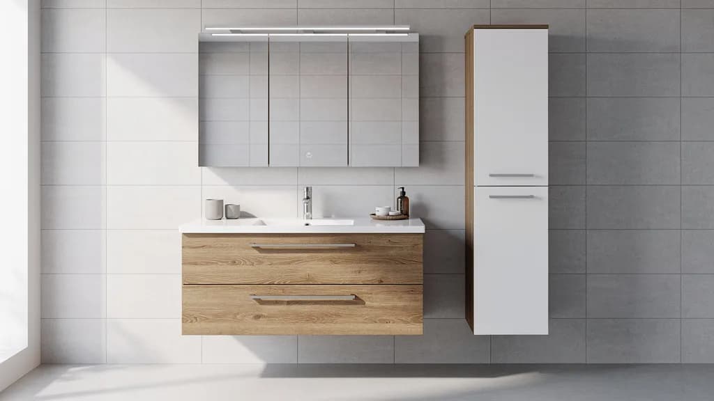 Wandmontiertes Badmöbel-Set aus einer Serie mit Waschtisch in Eiche-Optik, weißem Hochschrank und Spiegelschrank vor grauen Fliesen.