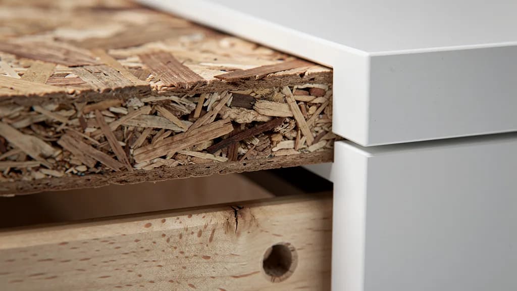 Querschnitt einer Spanplatte mit gepressten Holzspänen neben der Kante eines weißen Möbelstücks.