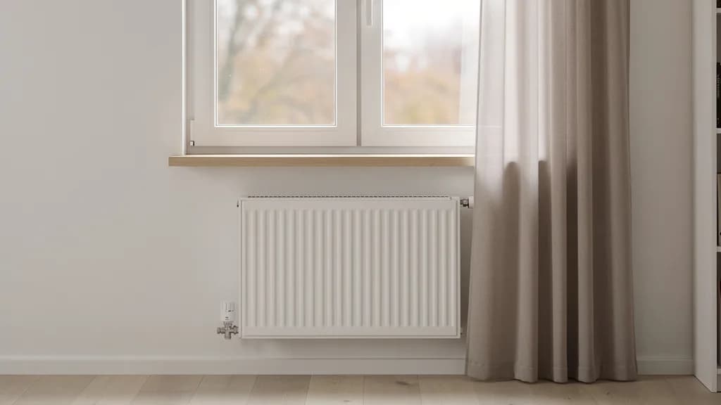 Wohnzimmerfenster mit Holzfensterbank, darunter ein frei stehender weißer Flachheizkörper, der Vorhang hängt seitlich neben dem Fenster