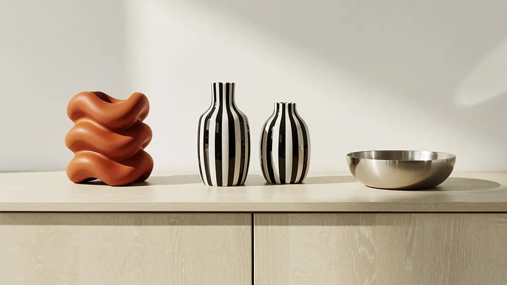 Orangefarbene Keramikskulptur, gestreifte Glasvasen und eine Edelstahlschale auf einem hellen Eichensideboard