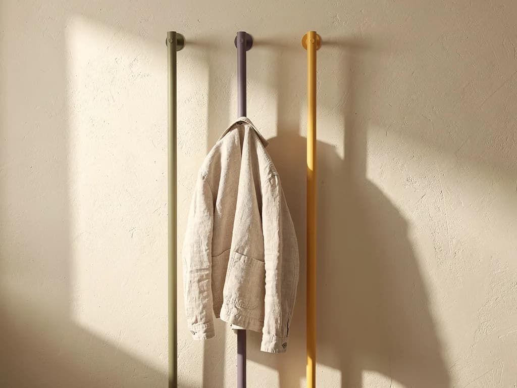 Drei Wandgarderoben-Stäbe in Oliv, gedämpftem Flieder und Blassgelb mit einer Leinenjacke.
